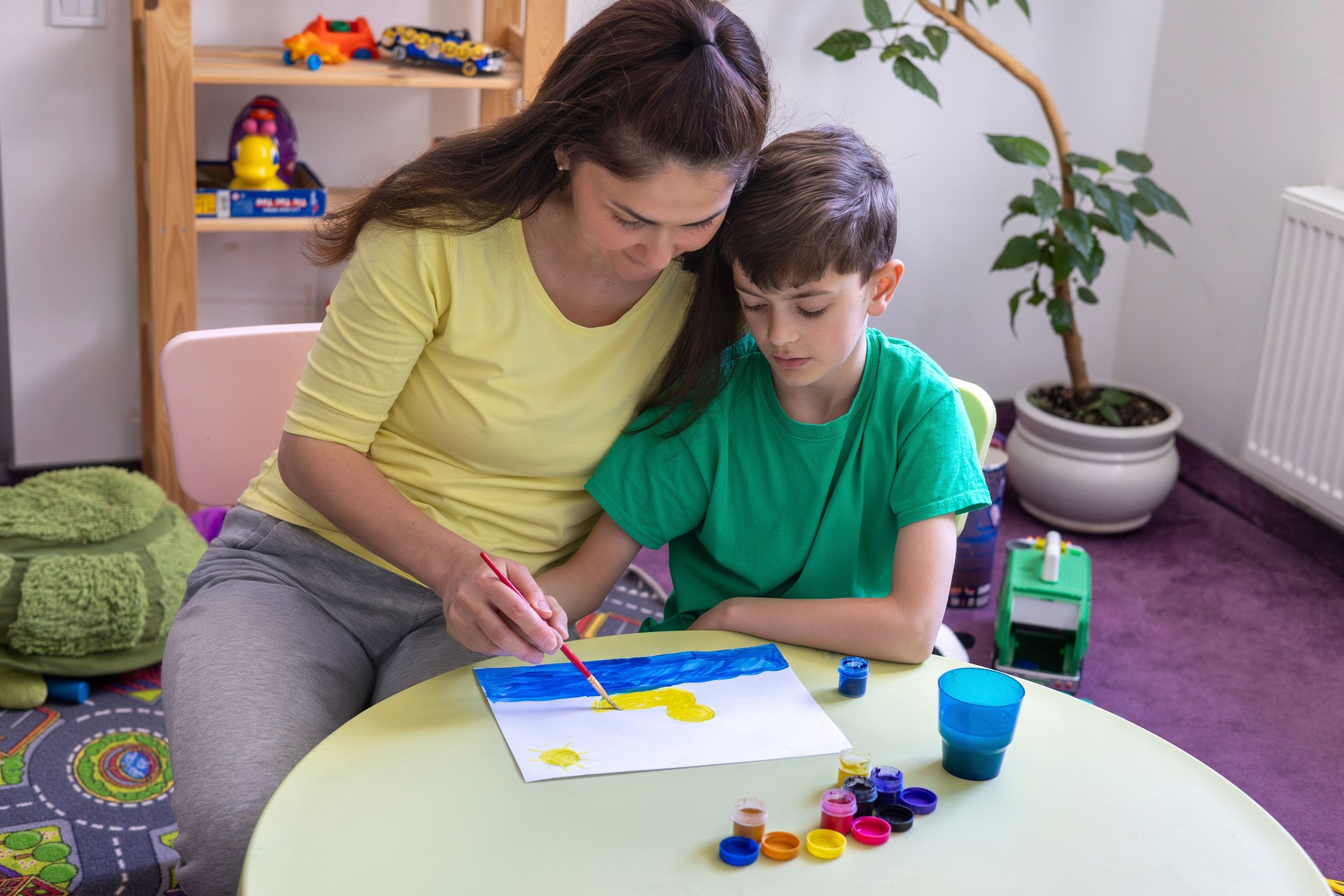 Art Therapy Session: Adult and Child Painting Together in Supportive Environment. Mom helps her son draw at home. Creativity, learning, family time. sensory activities for children with autism.
